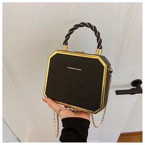 Gedetailleerd aanzicht van zwarte en gouden boxtas met gedraaid handvat en ketting.