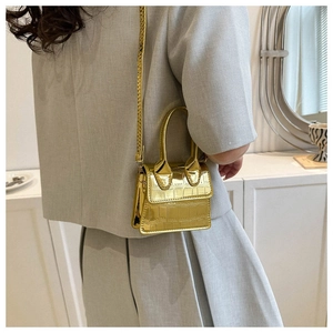 Close-up of a mini gold handbag with crocodile texture and thin shoulder strap