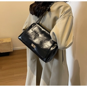 Detail of black patent leather crossbody bag with silver chain strap and metal buckle