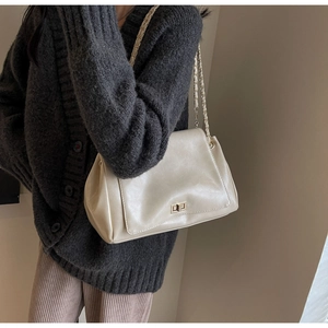 Detail of cream shoulder bag featuring gold twist lock and woven chain strap on model