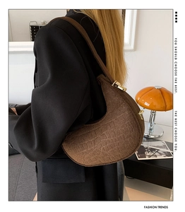 Detail of dark brown faux crocodile embossed crescent bag with gold buckle and strap
