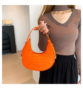 Model holding a bright orange felt crescent bag with crocodile pattern texture and gold buckle