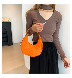 Detailed view of orange crescent bag featuring embossed crocodile pattern texture