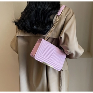 Detail of lavender quilted crossbody bag with gold chain strap worn over a trench coat