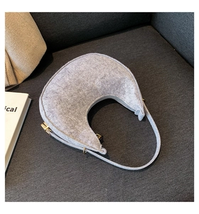 Detail of grey felt crescent bag with gold metal hardware and zipper on a soft sofa