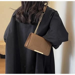 Brown chevron quilted crossbody bag with gold chain strap shown on a black winter coat