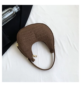 Detail of dark brown crescent bag with crocodile embossed texture and golden metal zipper