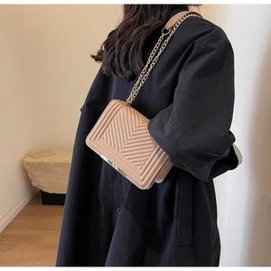 Close-up of beige quilted crossbody bag with V-stitch pattern and metal chain strap
