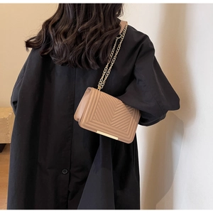 Detail of beige quilted shoulder bag with gold chain strap worn over a black winter coat