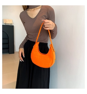 Detail of orange faux leather crescent bag with crocodile texture and gold hardware