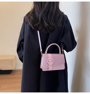 Vue arrière d'un sac bandoulière rose avec boucle carrée sur un manteau noir