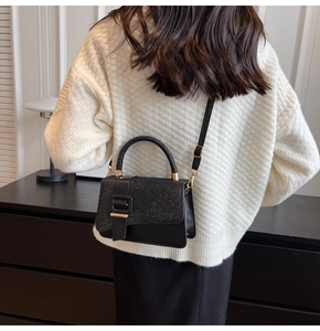 Détail d'un sac bandoulière noir avec texture pailletée et boucle dorée sur modèle