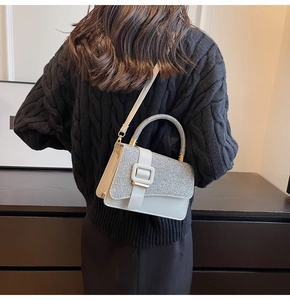 Sac à main blanc à paillettes avec boucle carrée porté par un mannequin en pull noir