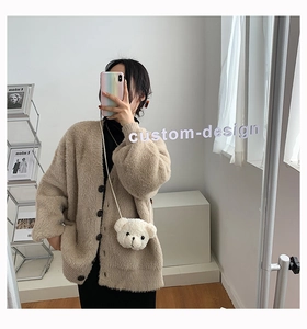 Dettaglio della borsa a tracolla in peluche a forma di orso bianco su cardigan beige