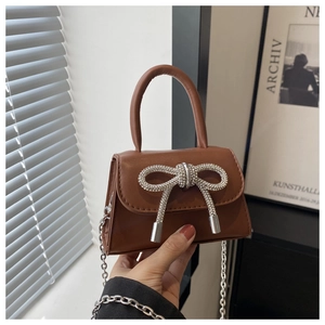 Détail du mini sac en cuir marron foncé avec nœud en strass et bandoulière chaîne argentée