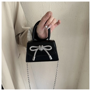 Detalle de mini bolso negro brillante con lazo de diamantes y cadena de plata