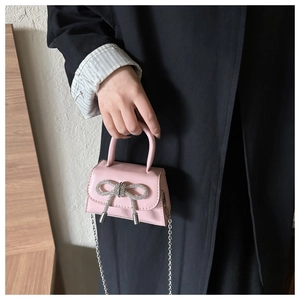 Detail of pink patent leather crossbody bag with silver rhinestone bow and chain strap