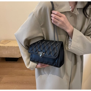 Dettaglio di una borsa a tracolla nera trapuntata con catena indossata su cappotto beige