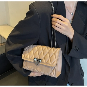 Dettaglio borsa trapuntata beige con catena e chiusura in metallo su blazer nero