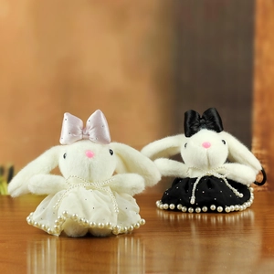 Detail of plush bunny charms with satin bows and pearl dresses on a wooden surface