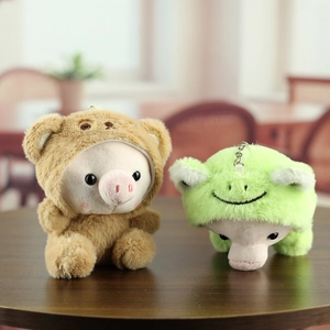 Détail de porte-clés en peluche cochon déguisés en ours et grenouille sur bois