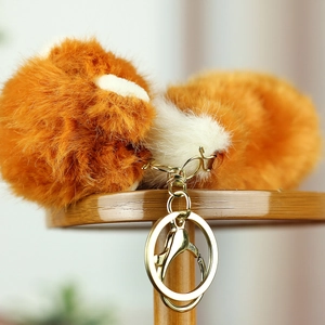 Close-up of a fluffy orange red panda plush keychain with gold lobster clasp on wood