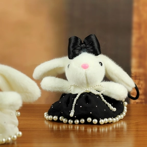 Close-up of white plush bunny pendant with black satin bow and pearl dress details