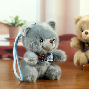 Close-up of a grey plush teddy bear with blue checkered bib and cherry detail