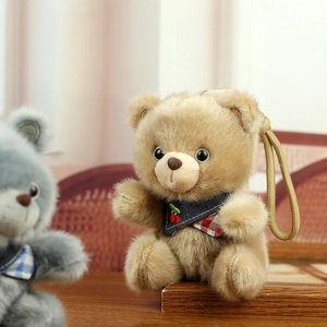 Close-up of cute plush bear charm with cherry scarf and khaki rope on a wooden desk