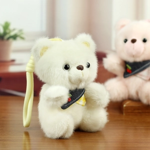 Close-up of a soft white plush bear keychain with a navy cherry bow tie and yellow strap
