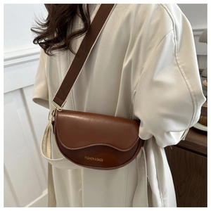 Détail d'un sac besace en cuir marron avec rabat festonné et large bandoulière sur un modèle