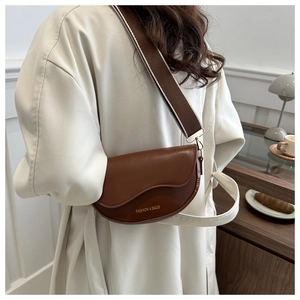 Détail du sac selle marron avec rabat ondulé et bandoulière en tissu tendance