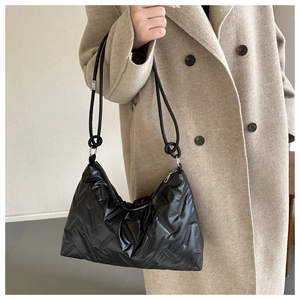 Detail of black quilted shoulder bag featuring rope strap knots on beige coat