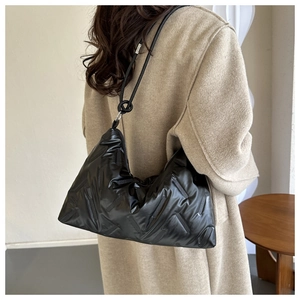 Detail of black quilted shoulder bag with knotted strap on a model wearing a beige coat