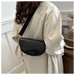 Gros plan du sac de selle noir avec large bandoulière tissée porté par un modèle
