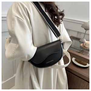 Détail du sac selle en cuir noir avec large bandoulière sur un mannequin en manteau blanc
