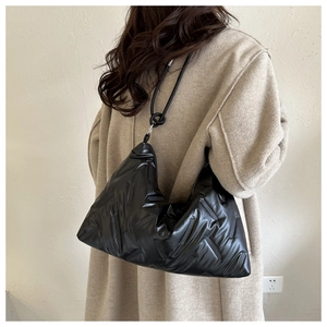 Detail of black puffer tote bag with knotted handle shown on model wearing a camel coat