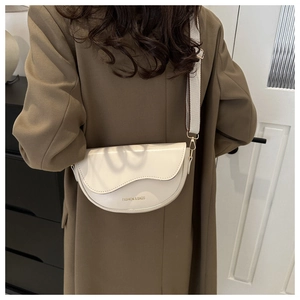 Détail d'un sac selle beige avec rabat ondulé et large bandoulière sur un manteau brun