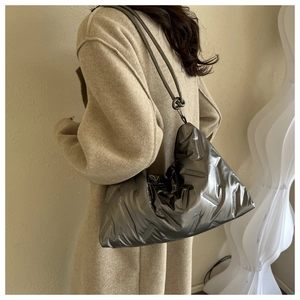 Detail of a large silver metallic puffer tote bag with quilted texture and knotted handles