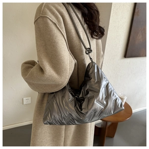 Silver quilted puffer tote bag shown on a model wearing a camel wool coat in a minimalist room