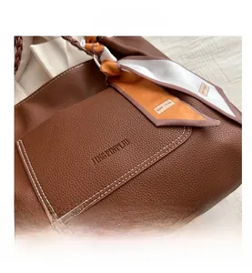Gros plan d'un sac cabas en cuir marron avec surpiqûres blanches et foulard en soie décoratif