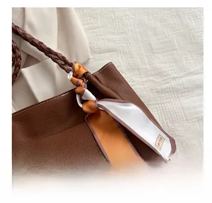 Détail du sac cabas en cuir grainé marron avec bandoulière tressée et foulard en soie
