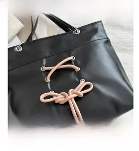 Détail d'un sac cabas noir avec nœud en cuir rose et œillets métalliques argentés