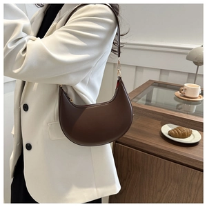 Gros plan sur le sac à main demi-lune en cuir marron porté avec un blazer blanc chic