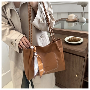 Detail of a brown leather tote bag with braided handles and decorative silk scarf