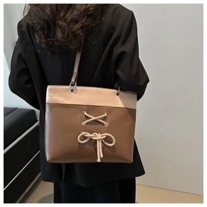 Détail du sac cabas bicolore avec nœud beige porté par un mannequin en blazer noir