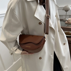 Sac besace marron en cuir avec large bandoulière, porté par un mannequin en café