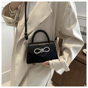 Detail van zwarte crossbody tas met zilveren strass strik op beige trenchcoat