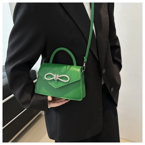 Detail van groene leren handtas met een sprankelende strass-strik en enveloppe flap