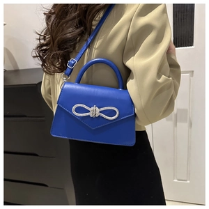 Detail van de helderblauwe crossbodytas met fonkelende zilveren strik en PU-leer